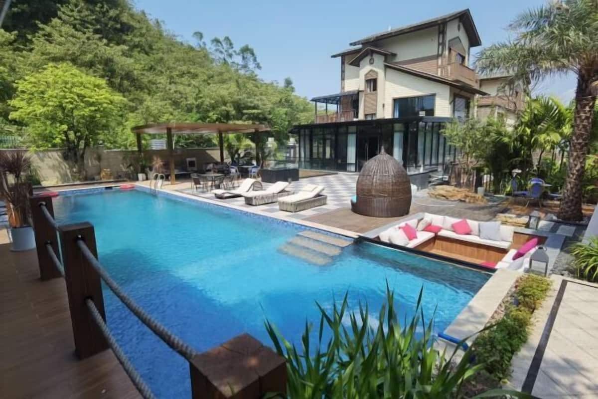 A swimming pool with lounge chairs, a pergola, and a modern house in the background.