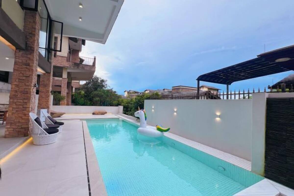 A modern pool area with a floating unicorn decoration, lounge chairs, and a stone pillar.