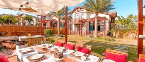 An outdoor dining area with a table set for four, surrounded by wooden chairs and red cushions.