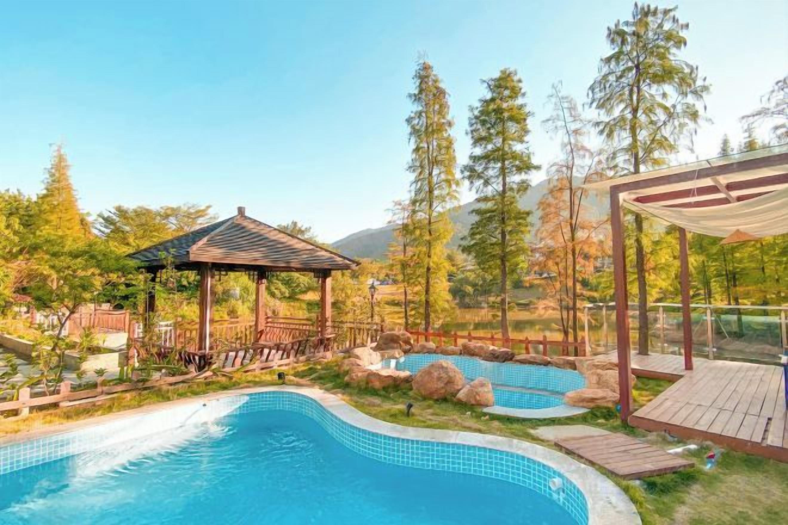 Una piscina con muelle de madera y un pabellón, rodeada de árboles y con una montaña al fondo.