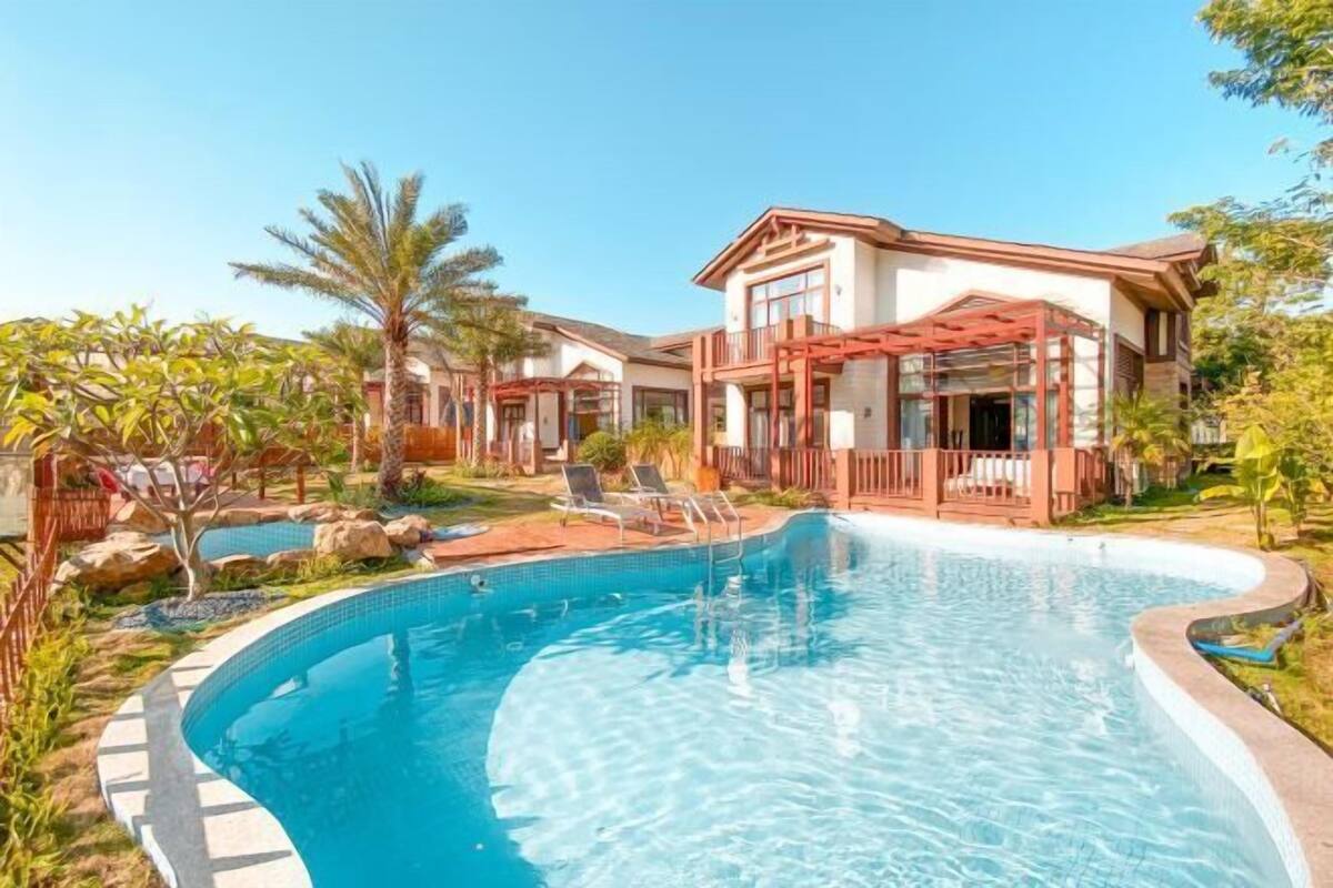 A swimming pool with a curved edge, surrounded by a wooden deck and lounge chairs.