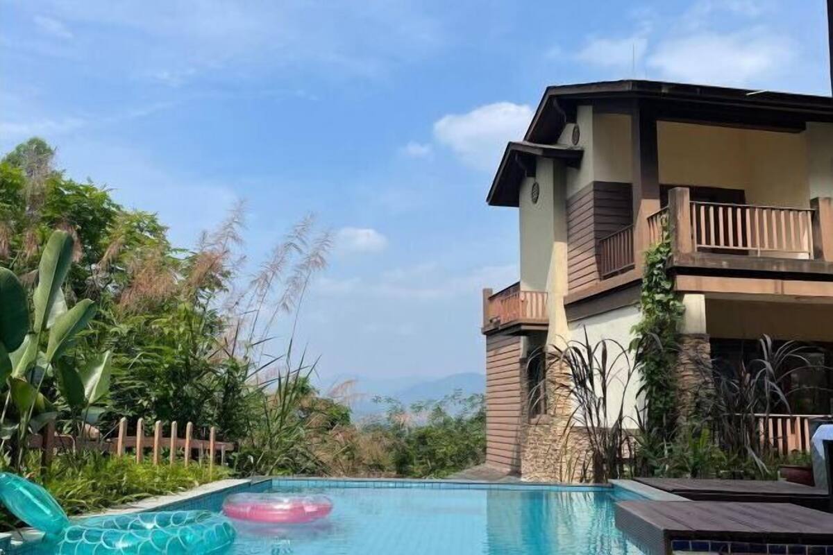 A pool area with a wooden deck, a lounge chair, and a view of a mountain range.