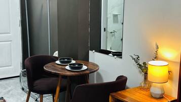 A room with a wooden table, two chairs, a mirror, a lamp, and a door.