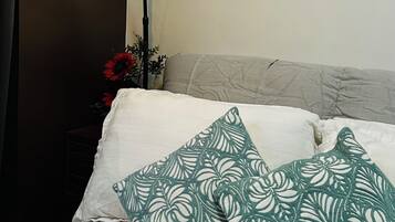 A bed with white bedding and green patterned pillows, a black floor lamp, and a wall with a dark panel.