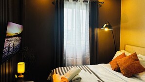 Hotellihuone, jossa on sänky, seinälle asennettu televisio, lamppu ja ikkuna, jossa on verhot.