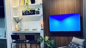 Moderni olohuone, jossa on litteänäyttöinen televisio, puupanelilla verhoiltu seinä ja ruokailutila, jossa on valkoinen työtaso ja baarituolit.