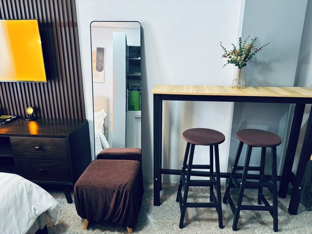 A bedroom with a bed, a dresser, a mirror, a desk with two stools, and a vase with flowers.