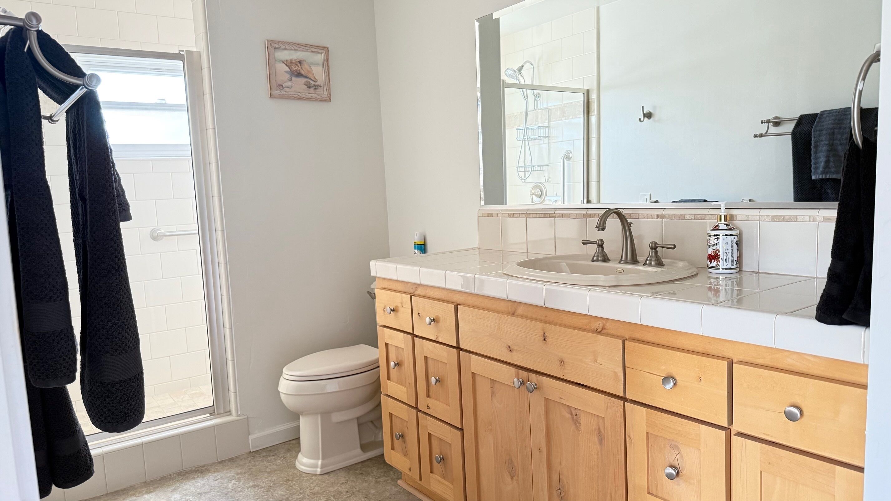 A bathroom with a toilet, sink, and wooden vanity with drawers. There is a towel rack with towels and a framed picture on the wall.