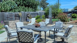 Un patio exterior con una mesa y sillas de piedra, rodeado por una valla de madera y vegetación.