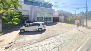 A modern building with a large glass facade, a parking area with two cars, and a paved walkway.