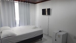 A bedroom with a bed, a TV mounted on the wall, and a small white cabinet.