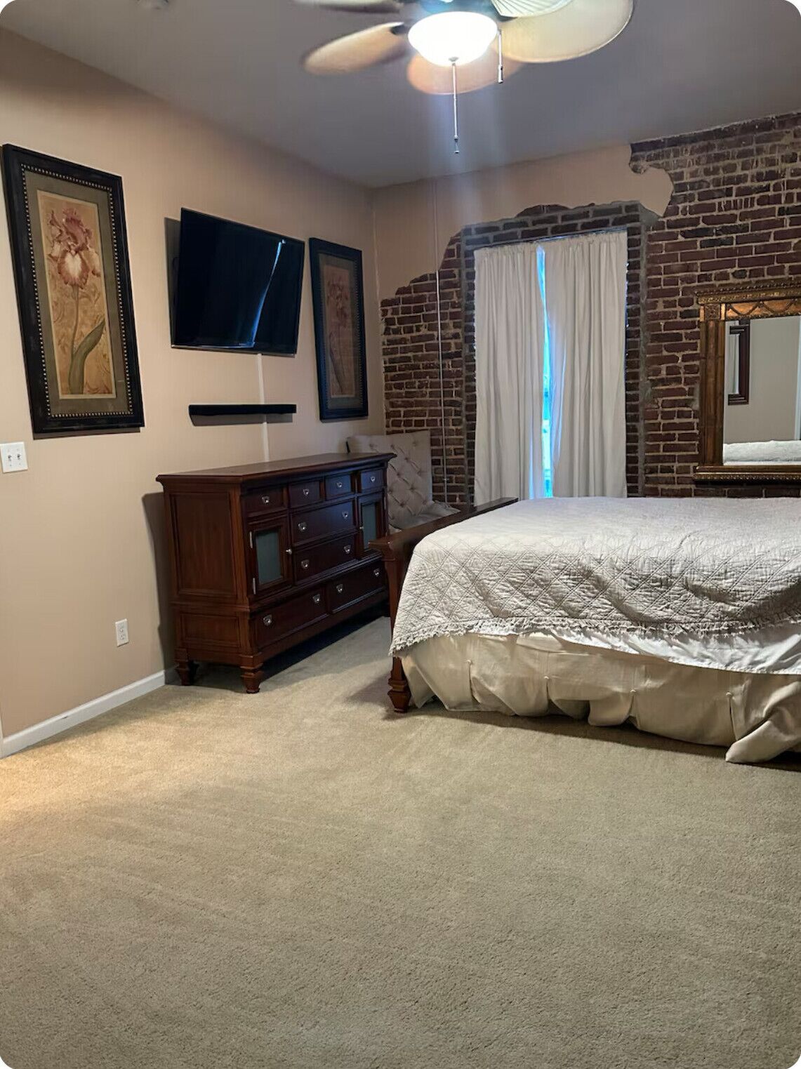 Un dormitorio con cama, cómoda, ventilador de techo y pared de ladrillo.