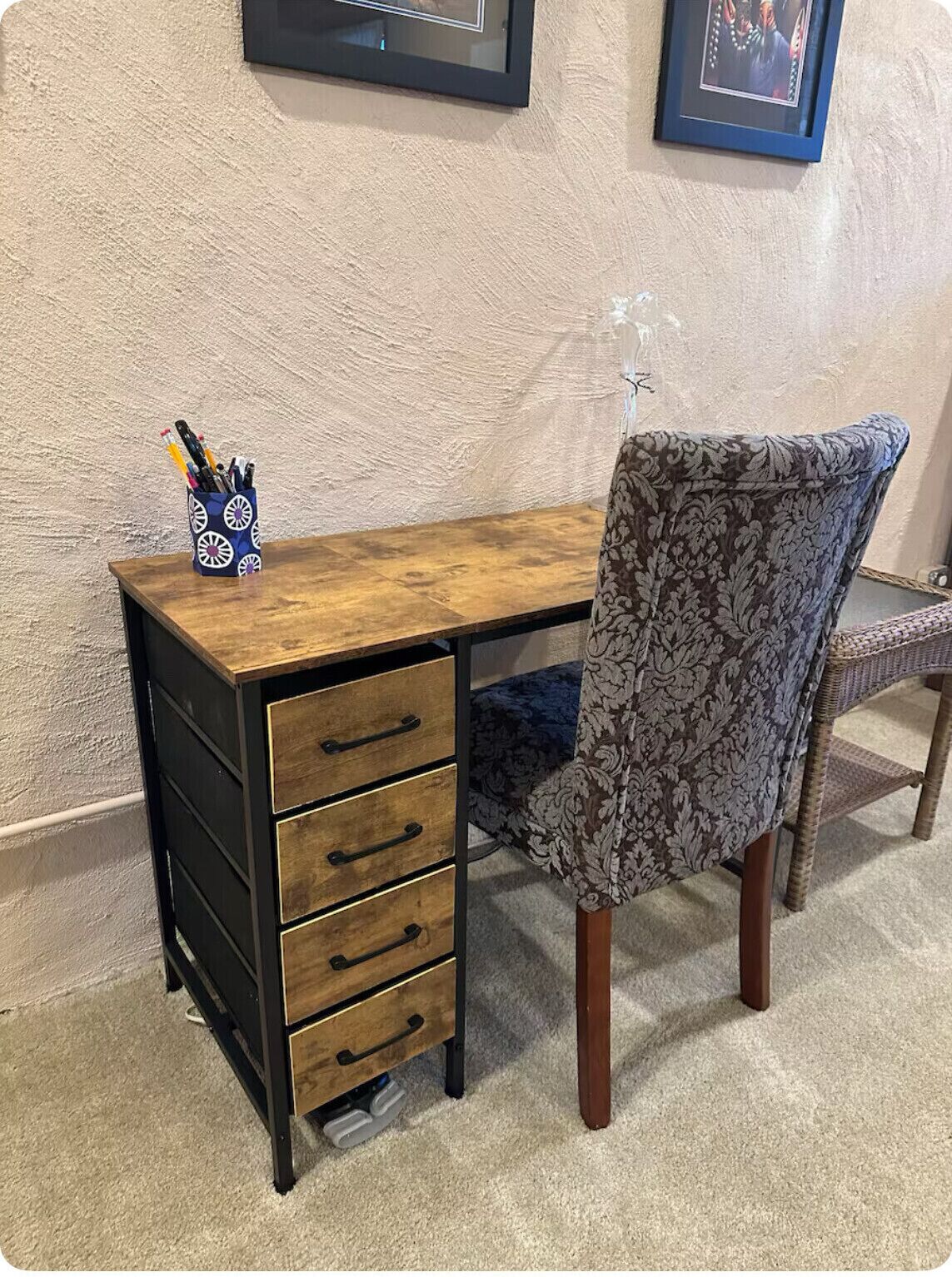 Un escritorio de madera con cajones negros y una silla con tela estampada.