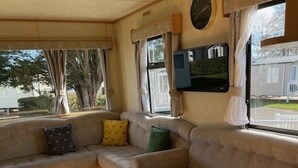A cozy RV interior with a sofa, a round table, and a TV mounted on the wall. - Home by the Sea - Adventure Village Access (Great Yarmouth)