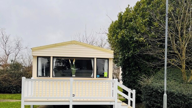 A small, single-story structure with a white exterior and a balcony. - Home by the Sea - Adventure Village Access (Great Yarmouth)