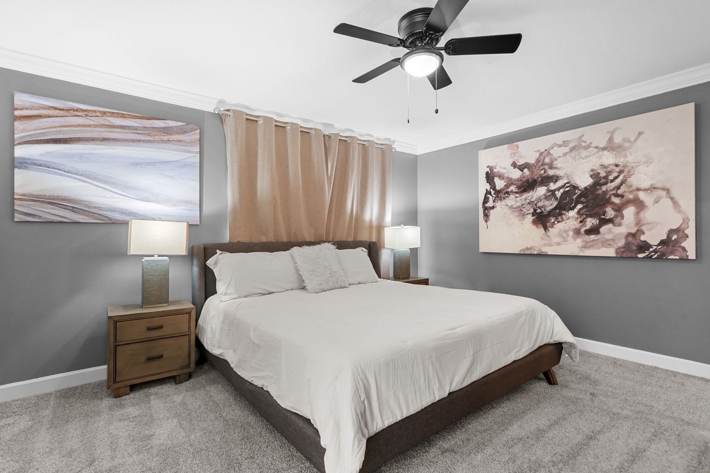 Una camera da letto con un letto, comodini, una ventola a soffitto e opere d'arte alle pareti.