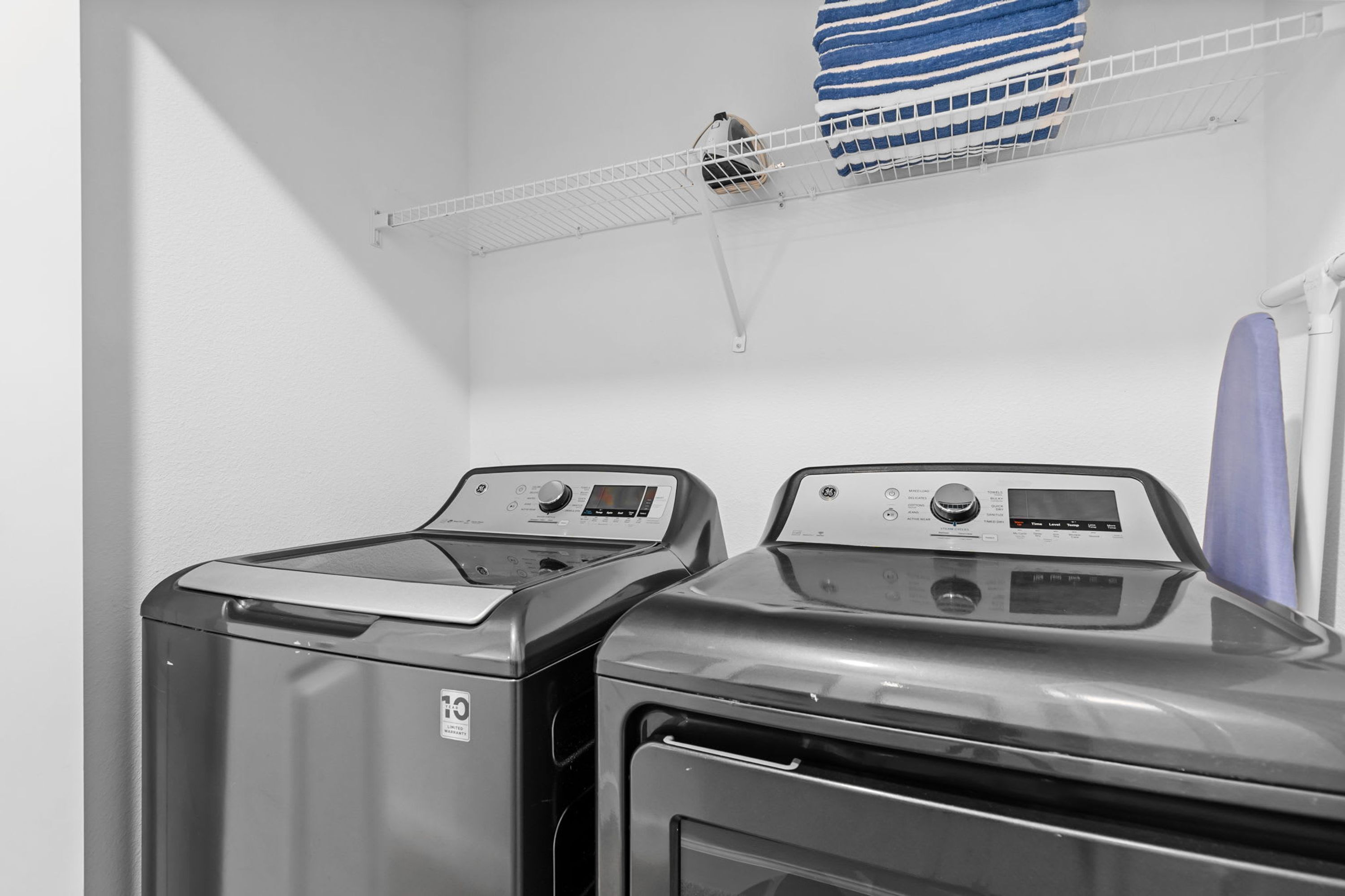 Two front-loading washing machines in a laundry room with a metal shelf above holding a folded towel.