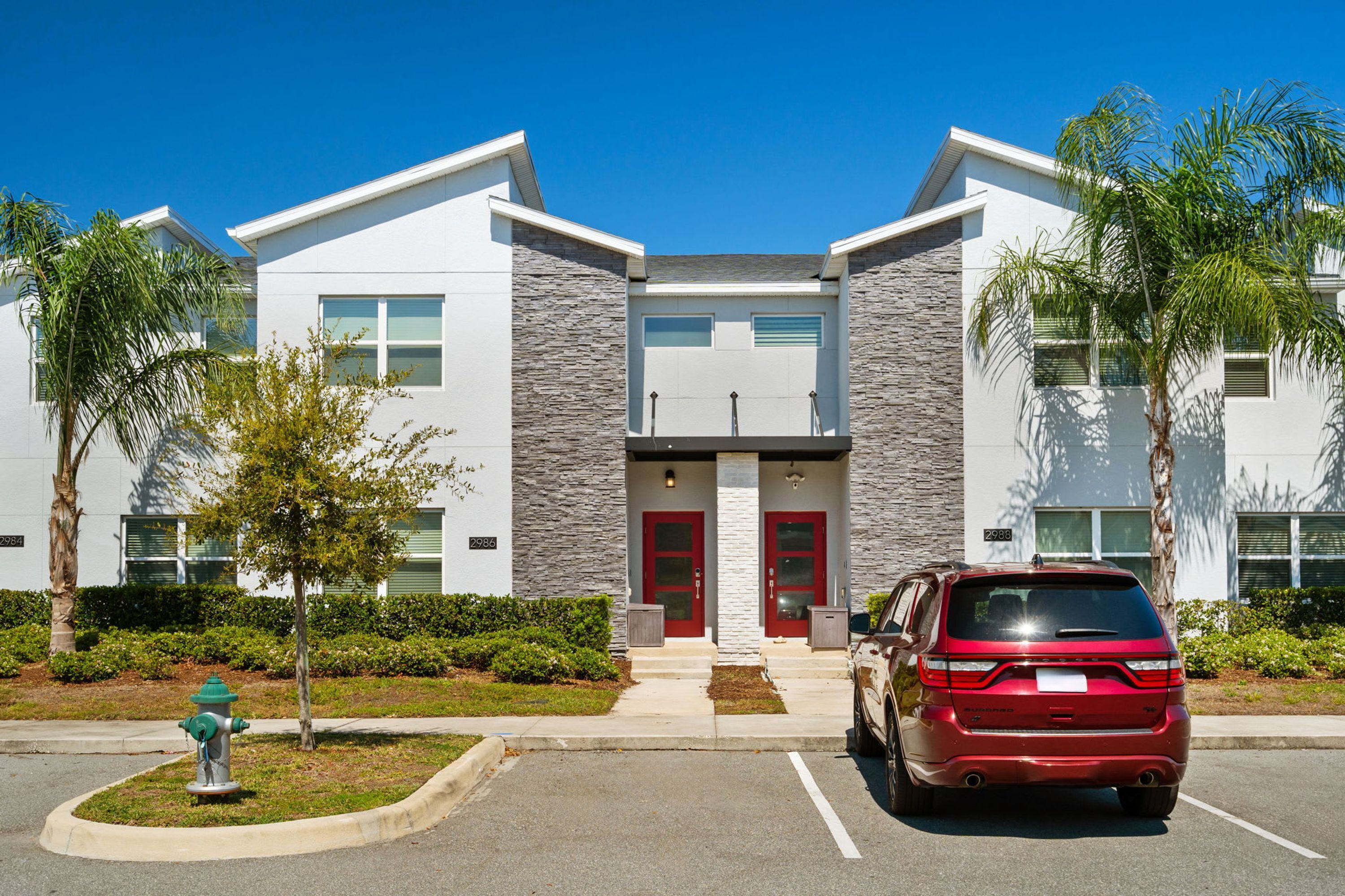 A modern building with a stone facade, red doors, and a parking lot with a red SUV.