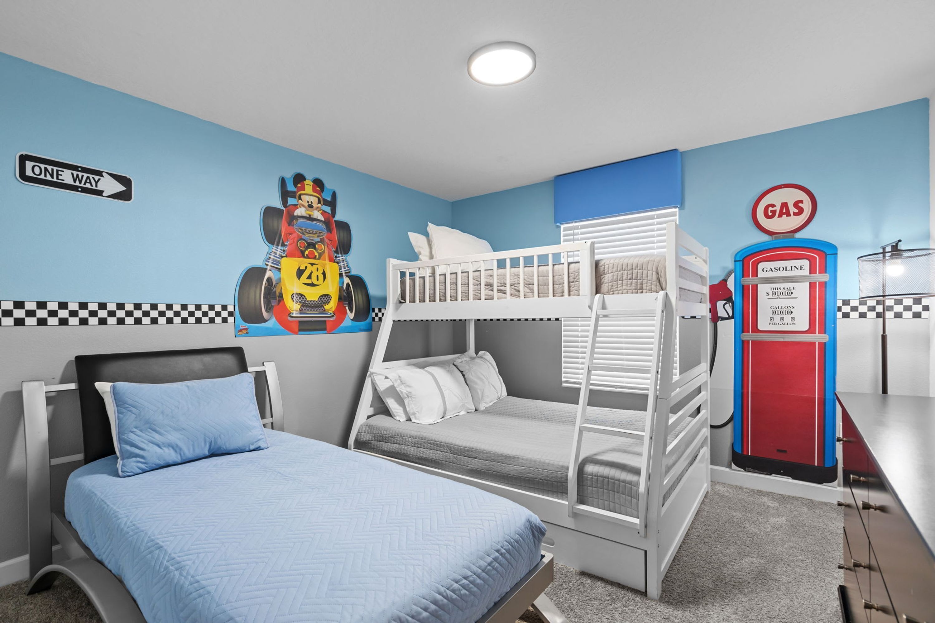 Quarto com uma cama de solteiro, uma cama individual, um mural de carro de corrida, um mural de bomba de gasolina e uma placa de sentido único.