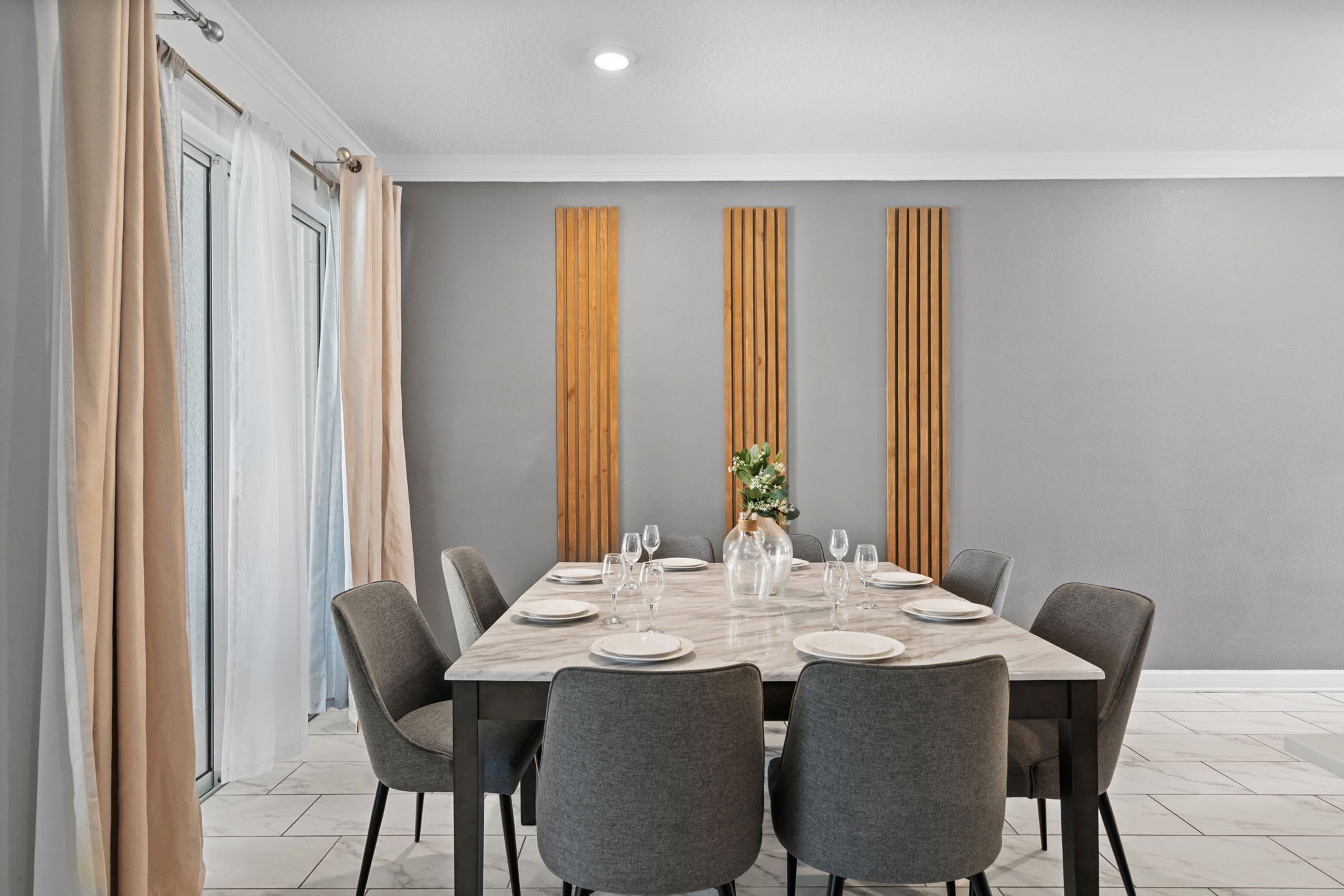 A modern dining area with a rectangular table set for six, surrounded by six grey chairs.