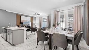 Una cocina moderna con una isla central, comedor con una mesa dispuesta para cuatro personas, y un ventanal con cortinas.
