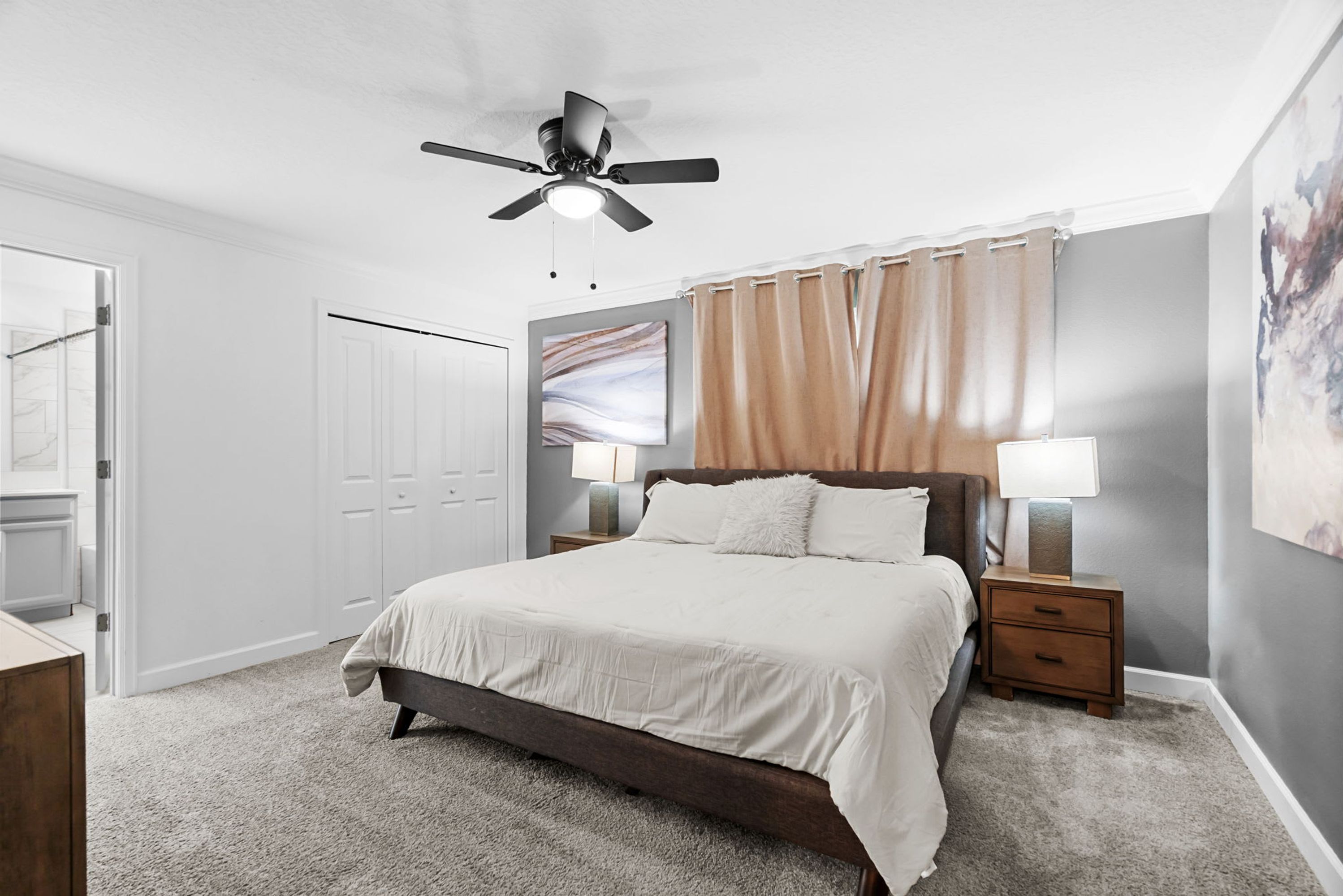 A bedroom with a bed, nightstands, a ceiling fan, a door, and a wall with a painting.