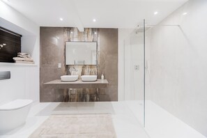 Ein modernes Badezimmer mit zwei Waschbecken, einer Duschkabine aus Glas und einer Marmor-Spritzschutzwand.