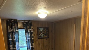 A bedroom with a bed, a painting on the wall, and a window with curtains. - Charming mobile home with WiFi and AC in lovely Cross Fork. (Cross Fork)