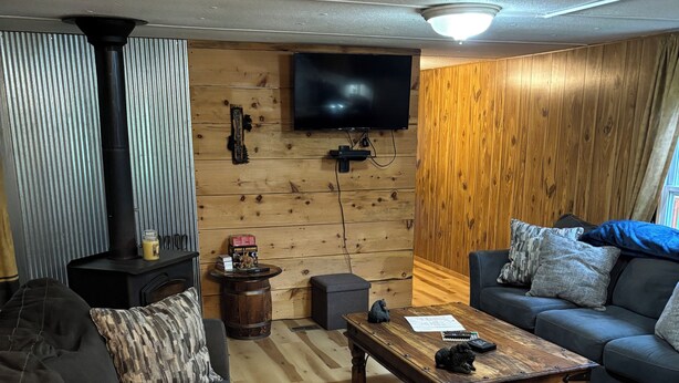 A cozy living room with a fireplace, a television mounted on the wall, a sofa, and a coffee table. - Charming mobile home with WiFi and AC in lovely Cross Fork. (Cross Fork)