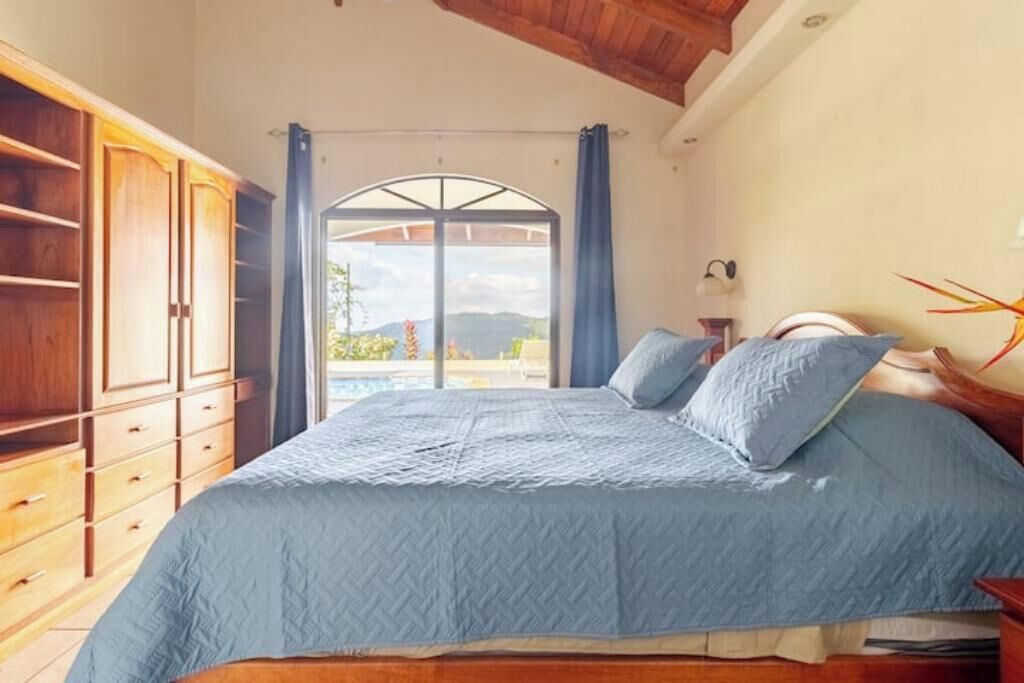 Camera da letto con un letto grande, un armadio in legno e vista sull'esterno tramite una porta vetrata.