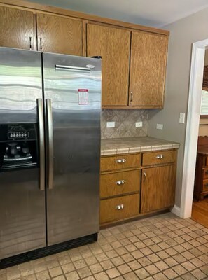 Una cocina con armarios de madera, un refrigerador de acero inoxidable y piso de baldosas.