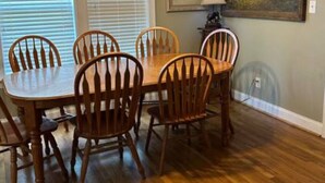 Une salle à manger avec une table et des chaises en bois, un lustre et un tableau au mur.