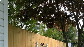 Une clôture en bois agrémentée d’un portail décoratif, une clôture blanche à piquets et une pelouse bien entretenue avec des plantes.