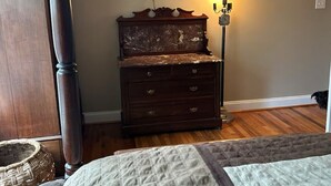 Une chambre à coucher comprenant un lit, une commode, un téléviseur fixé au mur et une lampe sur pied.