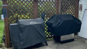 Two barbecue grills covered with protective tarps, a wooden lattice fence, and a weather vane in a backyard setting.