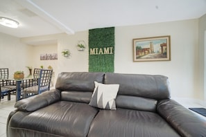 Un salon avec un canapé en cuir, une table à manger avec des chaises, un mur vert orné du mot « MIAMI » et un tableau encadré.