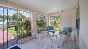 Un balcon avec des chaises en métal blanc, une petite table ronde et un fauteuil vert avec coussin.