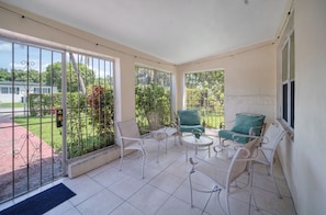 Un balcon avec des chaises en métal blanc, une petite table ronde et un fauteuil vert avec coussin.