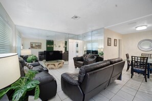 Een moderne woonkamer met een flatscreen televisie, leren banken, een glazen salontafel en een eetgedeelte met een glazen tafel en stoelen.