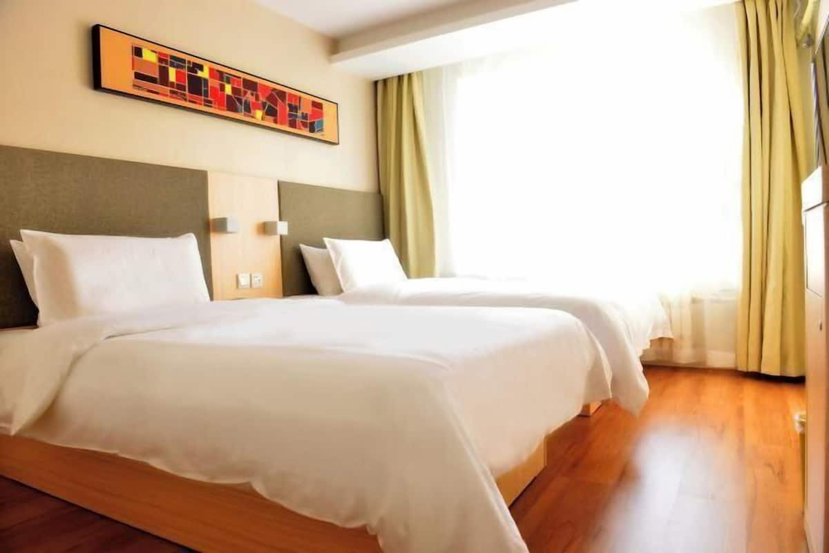 A hotel room with two beds, a large abstract painting on the wall, and a view of the outdoors through the window.