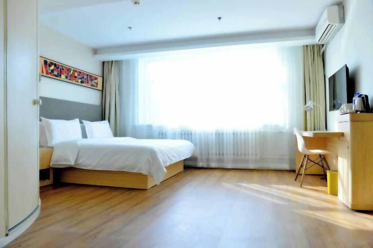 A hotel room with a bed, a desk, a chair, a TV, and a window with curtains.