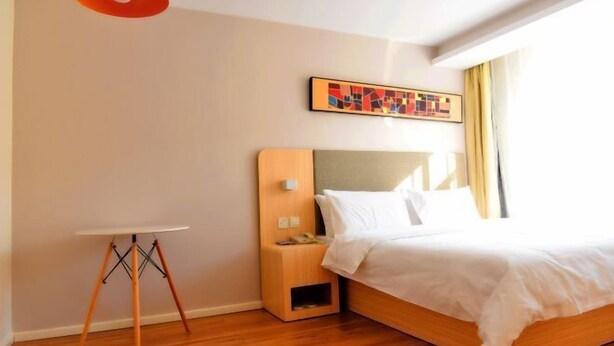 A hotel room with a wooden bed, a bedside table, a small wooden nightstand, a wall-mounted artwork, and a window with curtains. - HanTing Hotel (Yakeshi Xing'an Street) (Yakeshi)