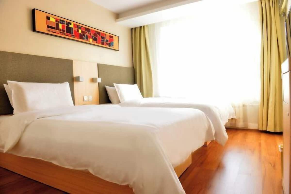 A hotel room with two beds, a large window with curtains, and a colorful abstract painting on the wall.