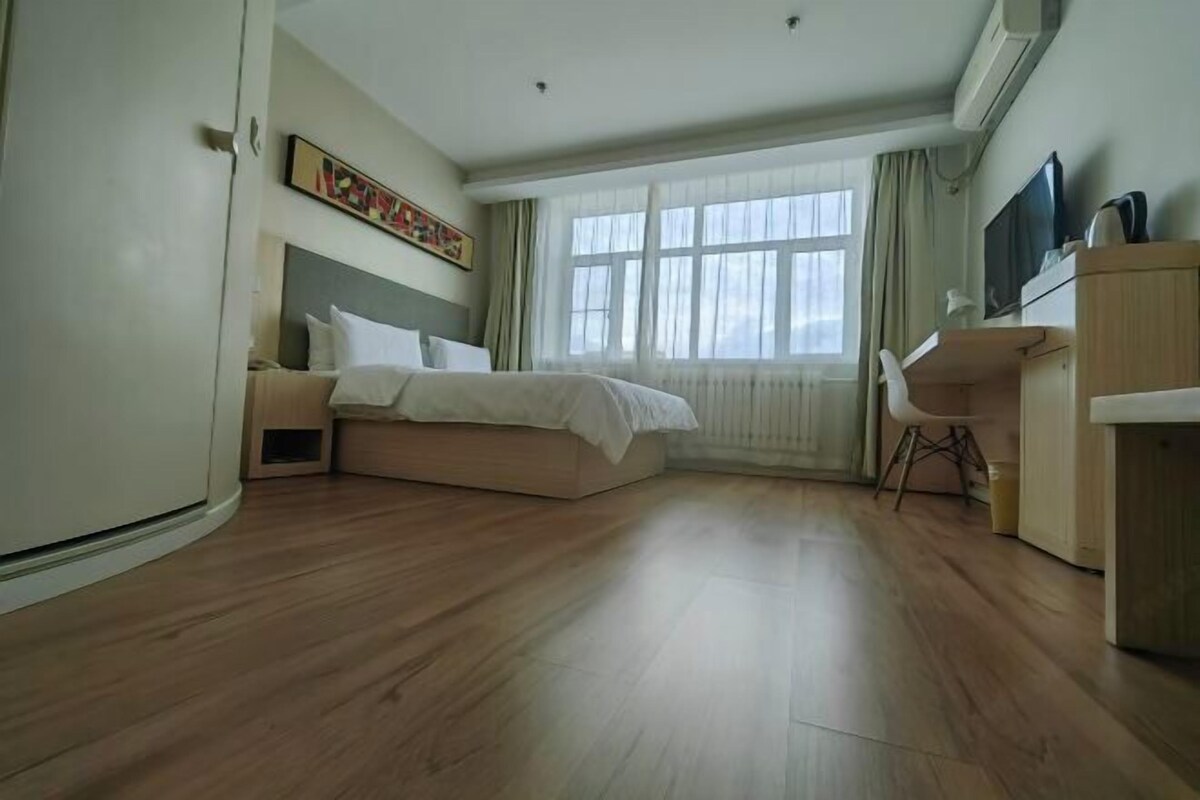 A bedroom with a bed, a desk, a chair, and a window with curtains.