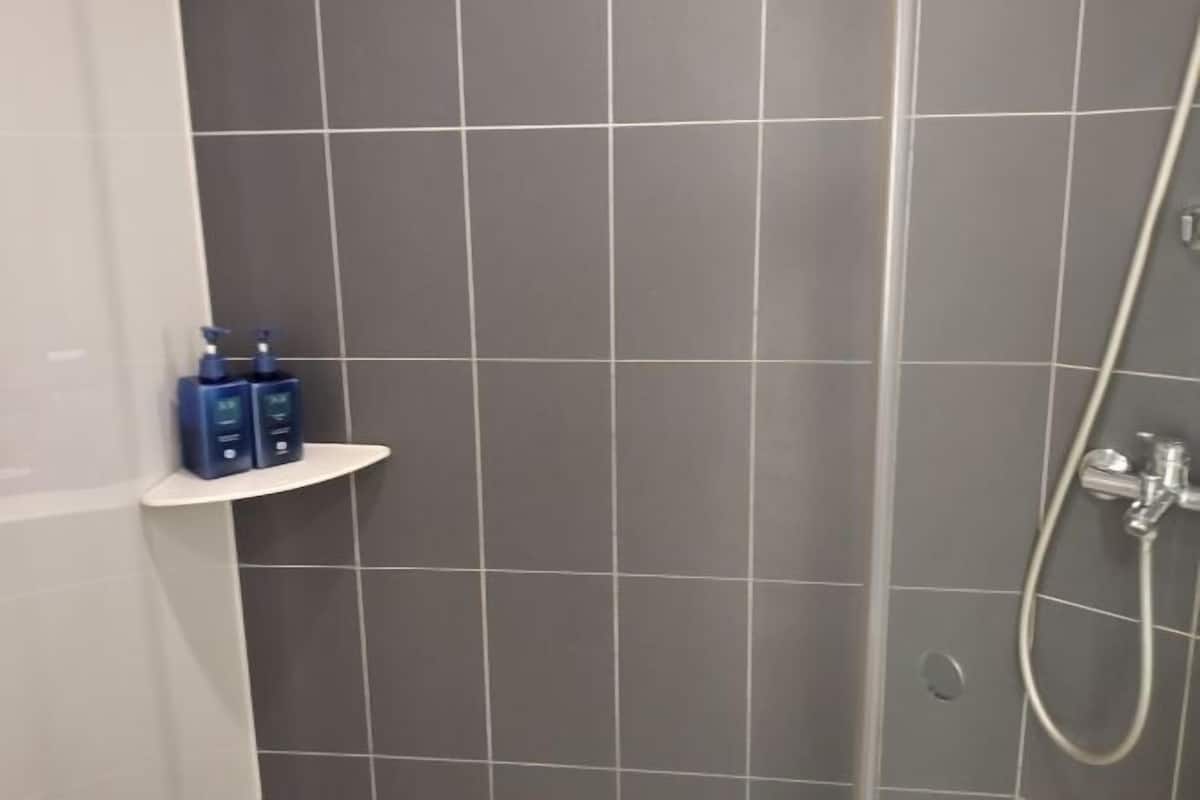 A bathroom with grey tiles, a shower, and a shelf with toiletries.