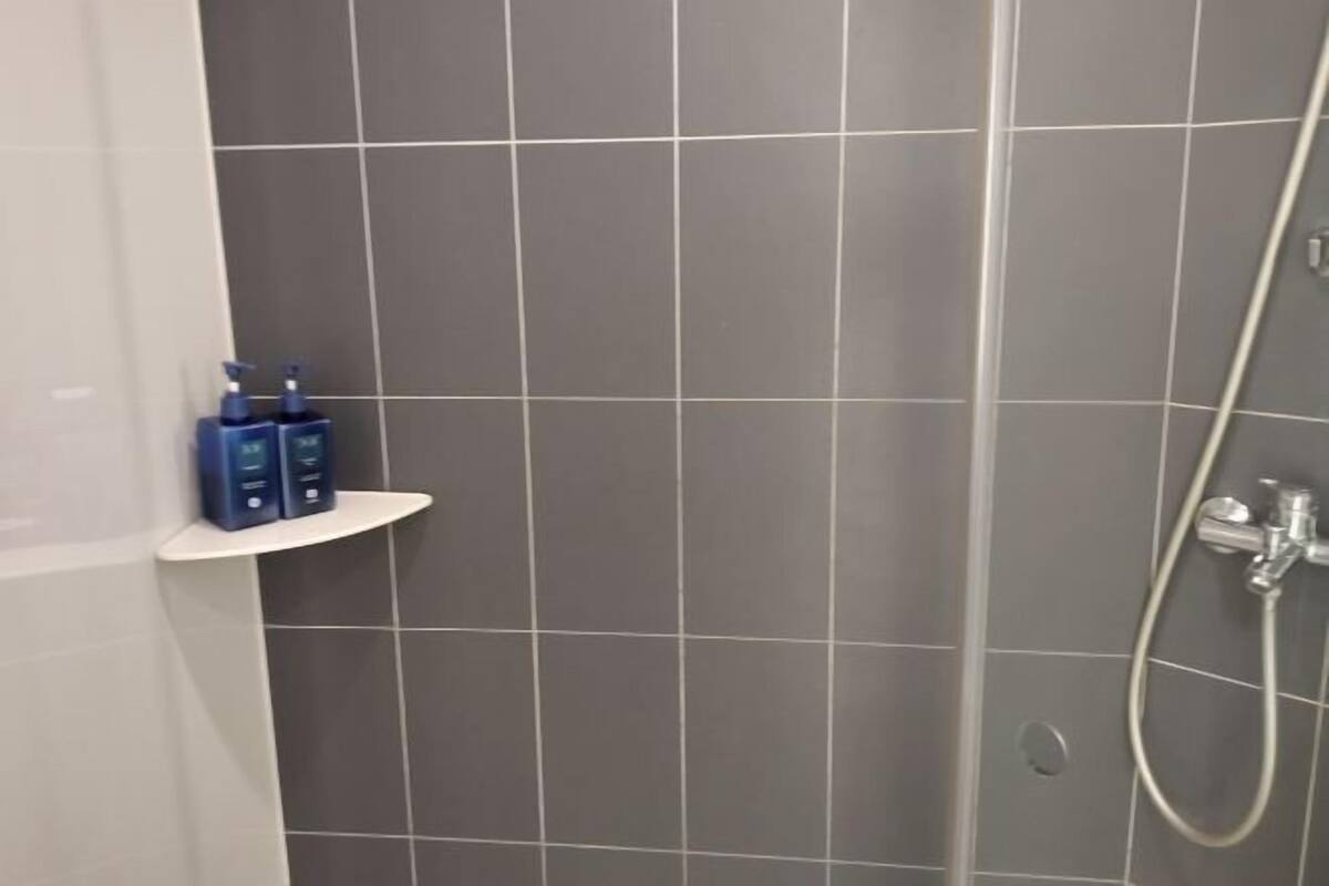 A bathroom with grey tiles, a shower, and a shelf with toiletries.