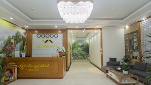 A hotel reception area with a wooden reception desk, a chandelier, a sofa, and a coffee table. - Viet Anh Ha Long Hotel (Bai Chay)