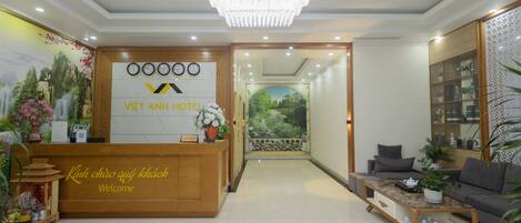 A hotel reception area with a wooden reception desk, a chandelier, a sofa, and a coffee table.