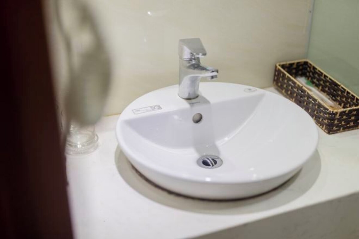 A white bathroom sink with a modern faucet, a small soap dish, and a wicker basket on the counter.