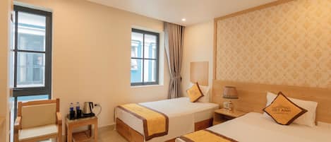 A hotel room with two beds, a chair, a small table with a kettle, and a nightstand with a lamp.